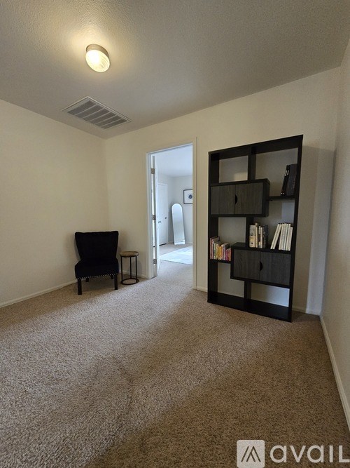 A room with a carpeted floor, a black chair, a black bookshelf, and a doorway leading to another room.