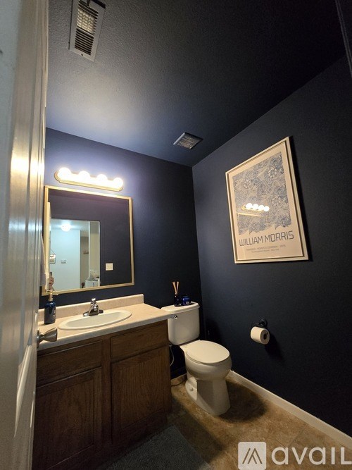 A bathroom with a toilet, sink, mirror, and a picture of William Morris.