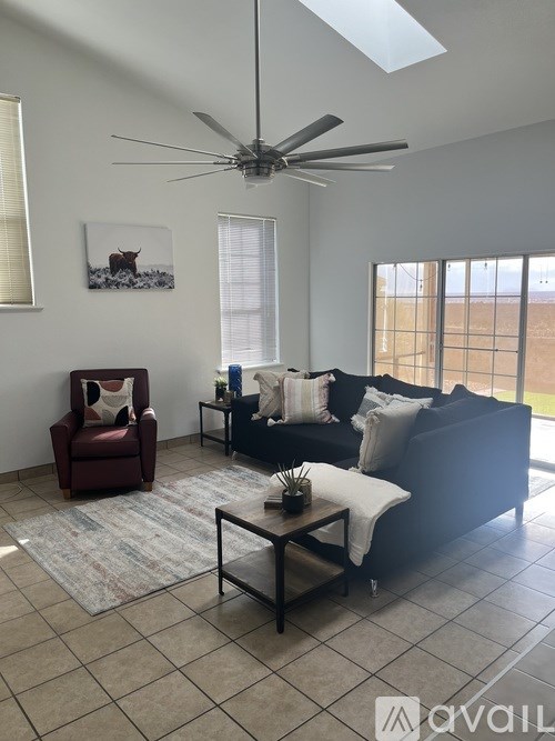 A living room with a black couch, a red chair, and a ceiling fan.