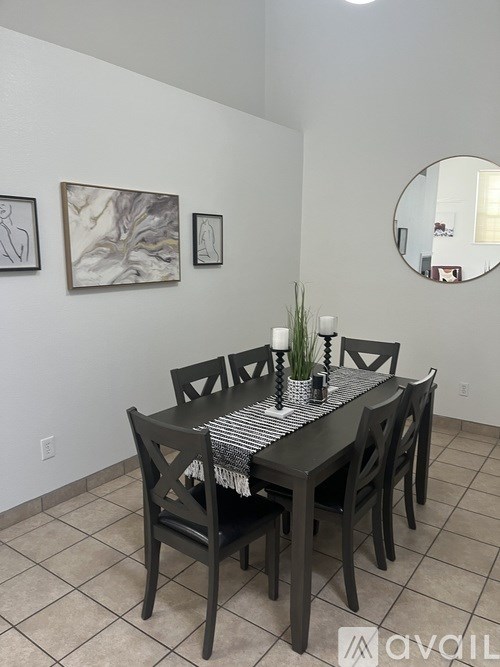 A black dining table with four chairs and a round mirror above it.