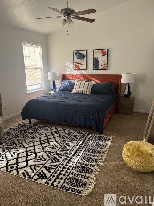 A bedroom with a bed, two lamps, a ceiling fan, and two paintings on the wall.