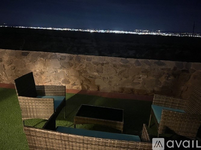 A patio with wicker furniture and a stone wall overlooks a city at night.