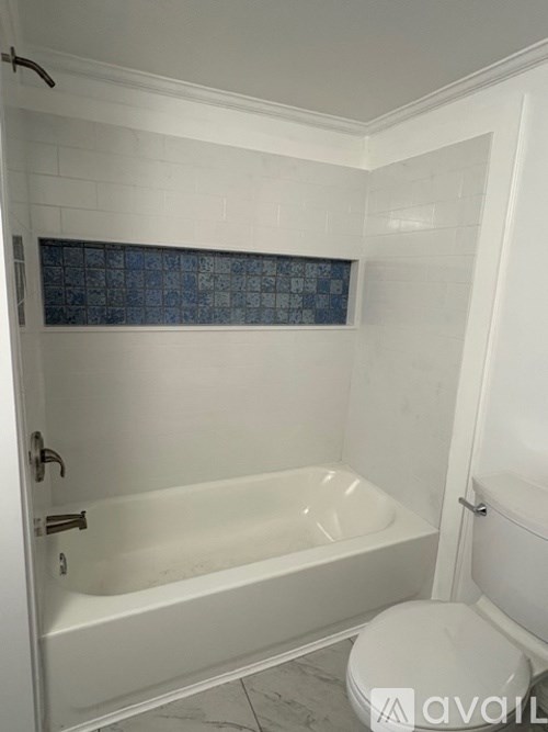 A white bathroom with a tub, toilet and a tile backsplash.