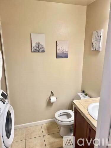 A small bathroom with a toilet, a washing machine, and two pictures on the wall.