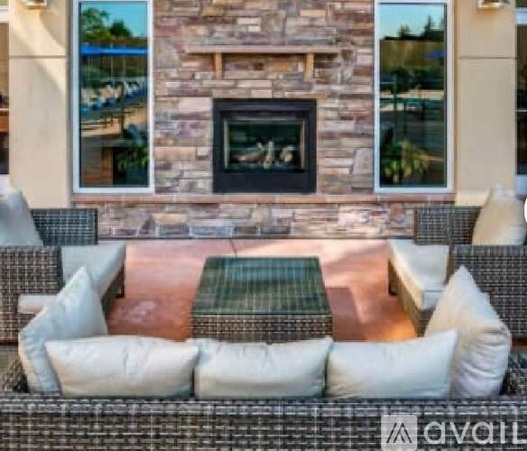 A patio with a stone fireplace and wicker furniture.