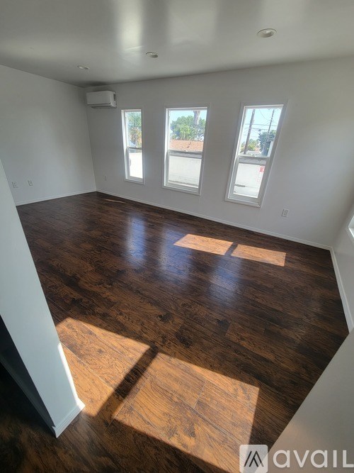 A room with wooden flooring and three windows.