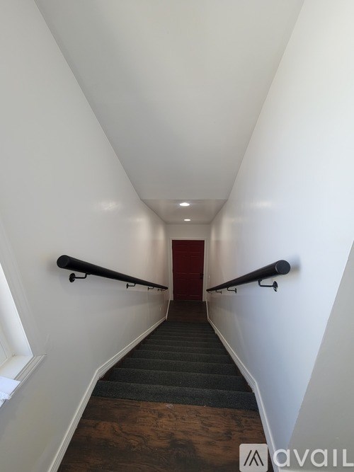 A long hallway with a staircase and a red door at the end.