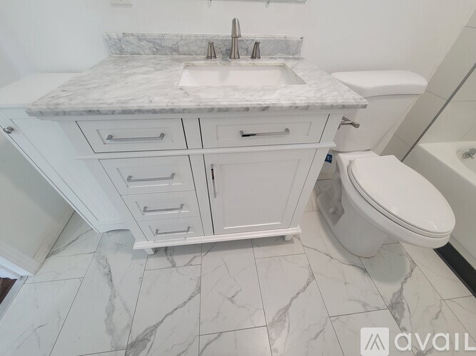 A white bathroom with a marble countertop and a toilet.