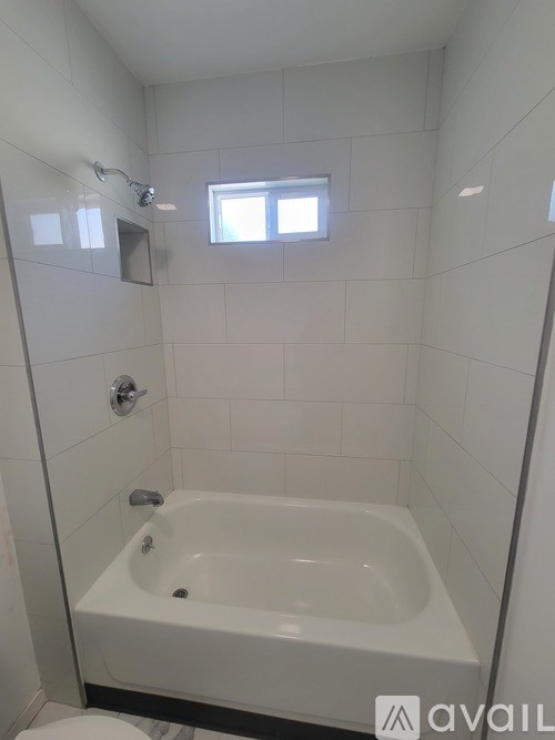 A white bathroom with a tub, toilet and window.