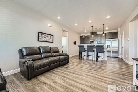 A black leather sofa sits in a spacious living room with wooden flooring and a framed "HOME" sign on the wall.