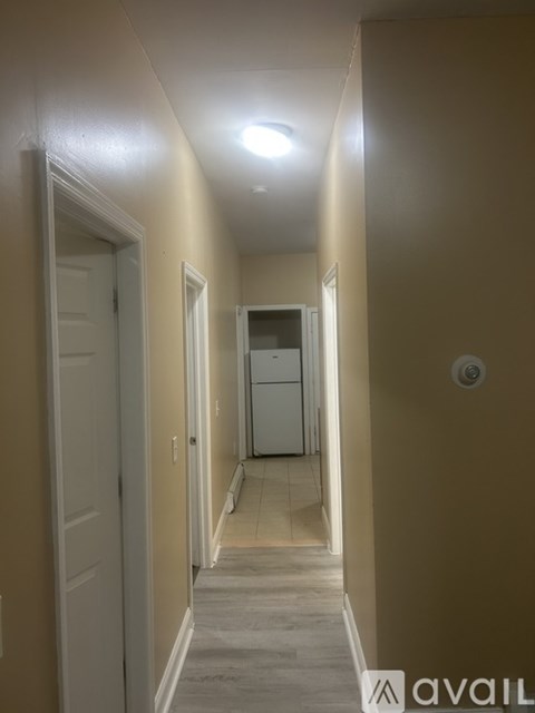 A long hallway with a white door on the left and a white cabinet on the right.