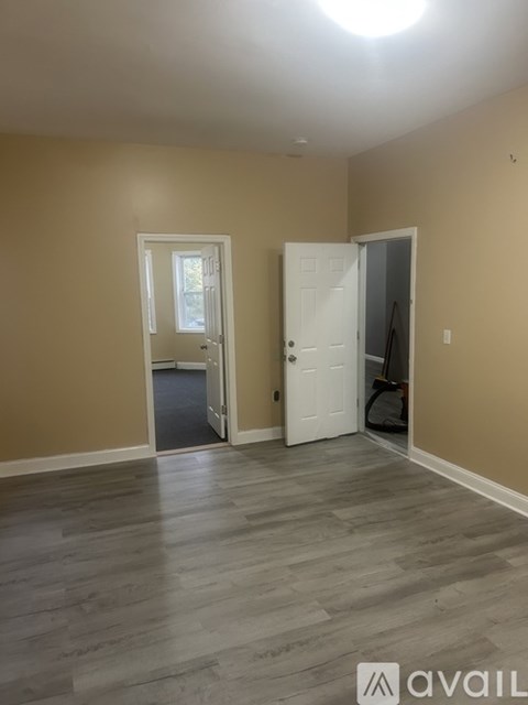 A room with a white door and a window with a view of trees.