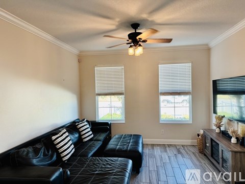 A living room with a black leather couch and a ceiling fan.