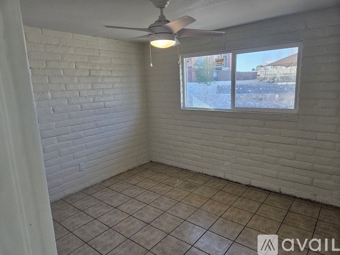 A room with a ceiling fan and a window overlooking a street.