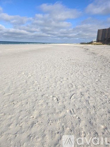 A sandy beach with footprints in the sand leading to a building in the distance.