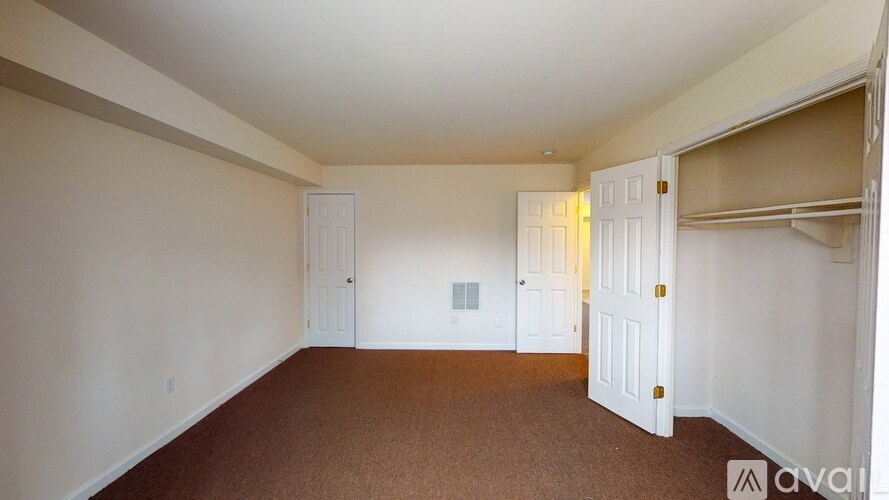A room with white walls and brown carpeting is available for rent.