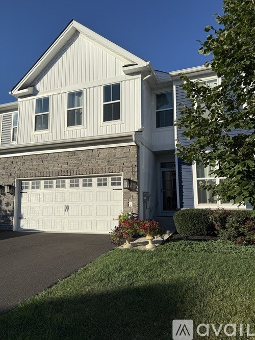 A white house with a garage door and a tree in front.