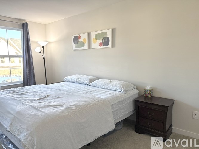 A bedroom with a white bed and a nightstand with a lamp.