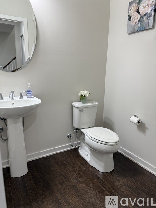A white toilet with a white sink and a white flower in a vase.