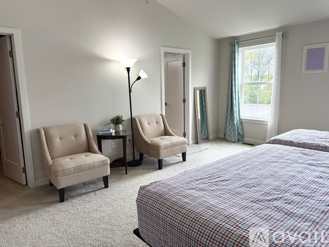 A bedroom with a bed, two chairs, and a lamp.