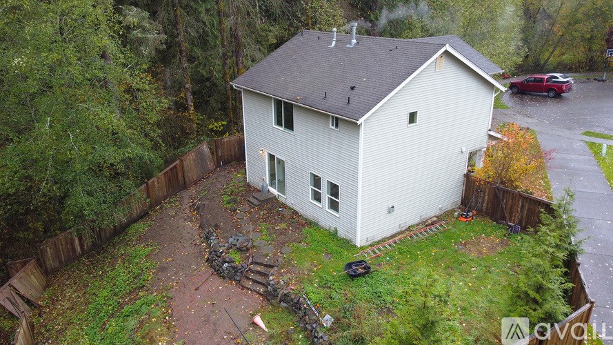 A house with a grey roof and white walls is surrounded by a fence and trees.