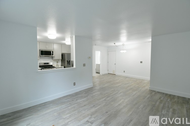 A spacious room with wooden flooring and a kitchen visible through a window.