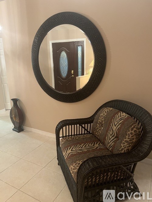 A wicker chair with a patterned cushion sits in front of a round mirror.