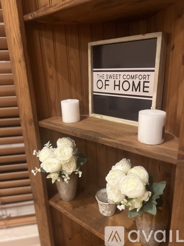 A wooden shelf with a sign that says "The Sweet Comfort of Home" and some flowers.