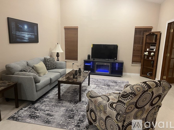 A living room with a grey couch, a coffee table, a television, and a patterned armchair.