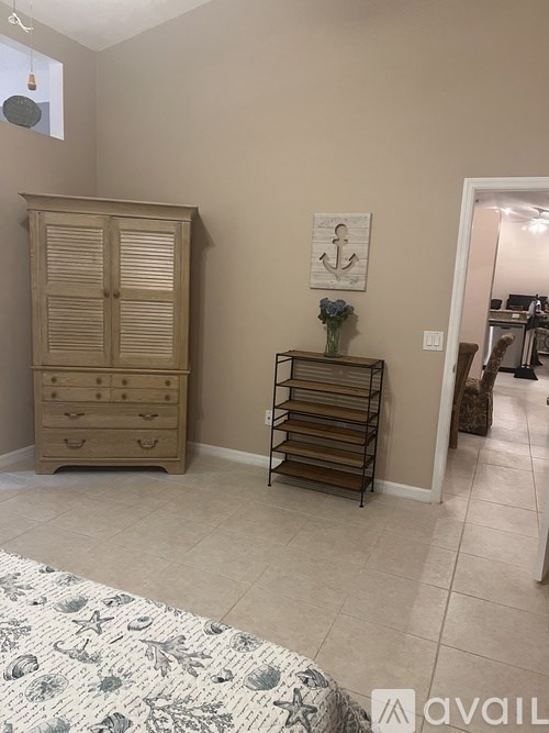 A room with a wooden wardrobe, a small table with a vase of flowers, and a painting of an anchor on the wall.