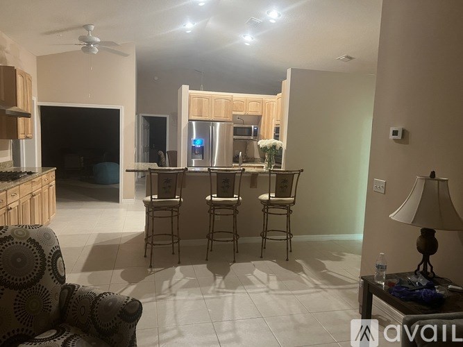 A living room with a grey sofa, a wooden cabinet, a television, a dining table with four chairs, and a ceiling fan.
