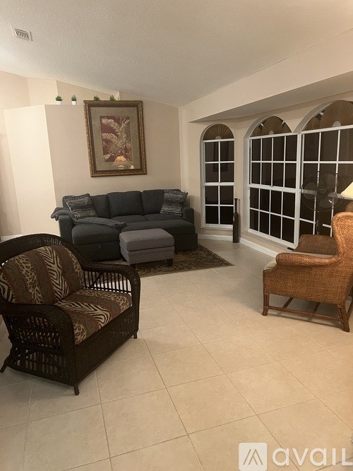 A living room with a sofa, two chairs, and a fan.