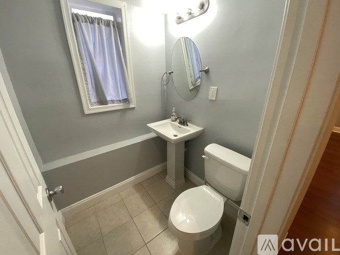 A bathroom with a toilet, sink, mirror, and light.