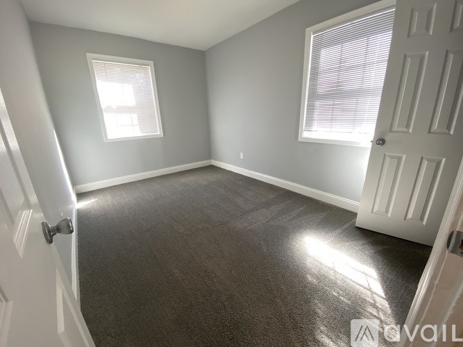 A room with a carpeted floor, two windows, and a door.