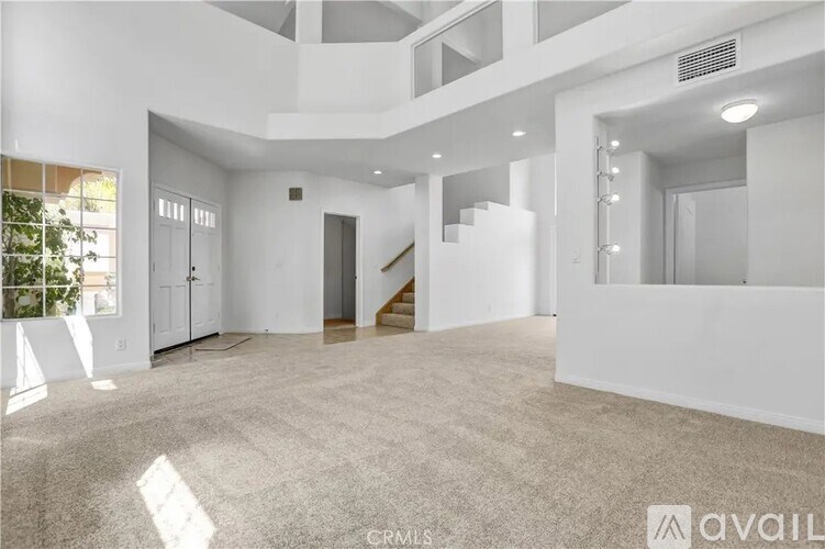 A spacious, well-lit living room with a carpeted floor and a staircase leading to another level.