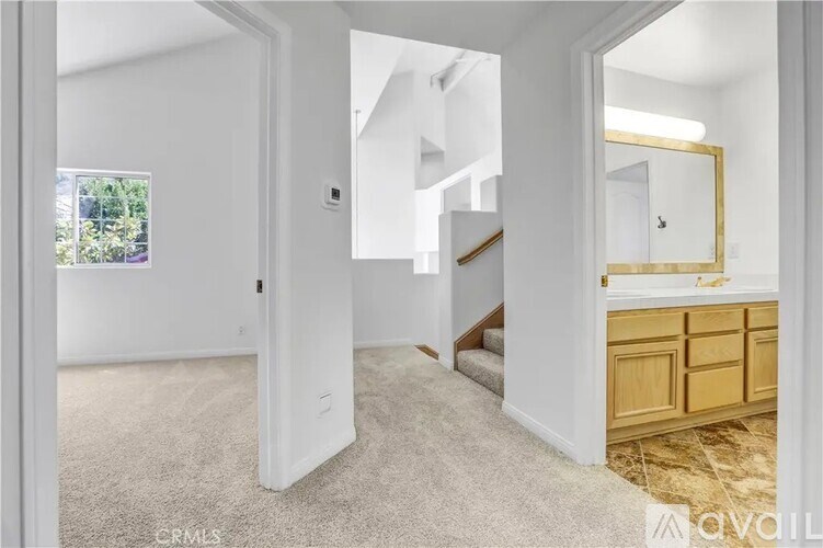 A spacious room with a carpeted floor, a staircase, and a mirror on the wall.