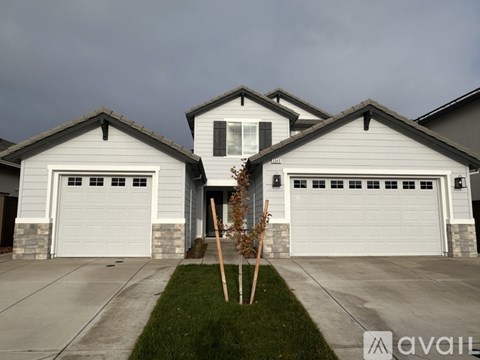 A house with two garages and a front yard with a small tree.