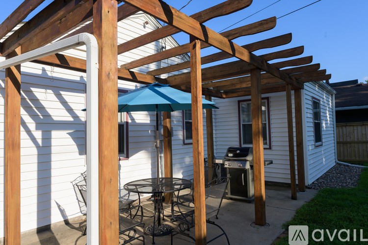 A wooden pergola with a blue umbrella is over a patio table.