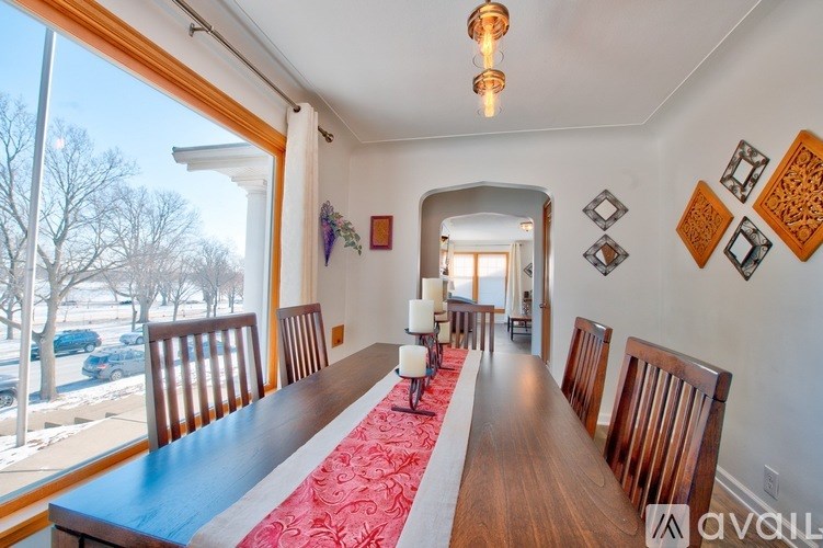 A long wooden table with chairs and a red runner is in a room with a large window.