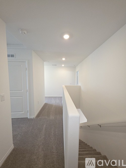 A hallway with a carpeted floor and a staircase on the right side.