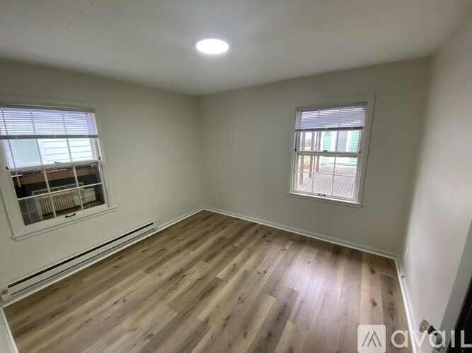 A room with wooden flooring and two windows.