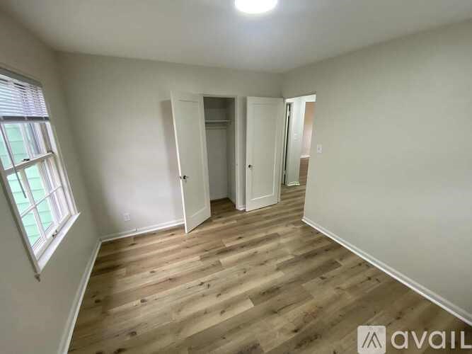 A room with wooden flooring and white walls, with a window on the left and a door on the right.