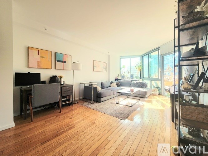 A living room with a grey couch, a wooden floor, and a painting on the wall.
