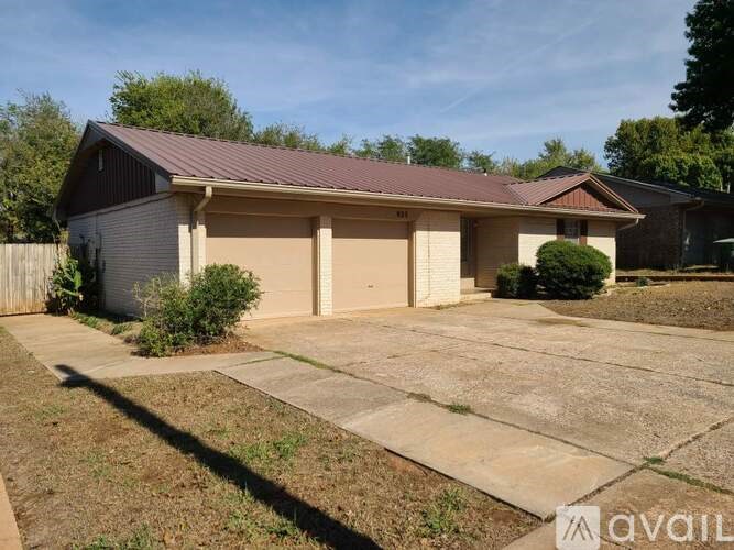 A house with a brown roof and a garage door is surrounded by a concrete driveway and a small garden.