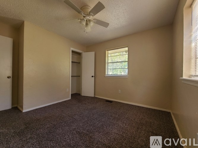 A room with a carpeted floor, a ceiling fan, and a window with blinds.