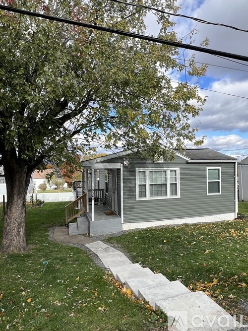 A small house with a grey roof and a tree in front of it.