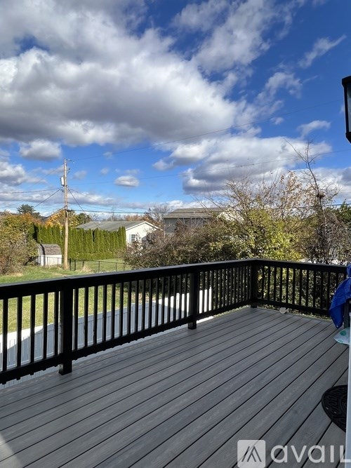 A wooden deck with a black railing and a view of the sky and trees.