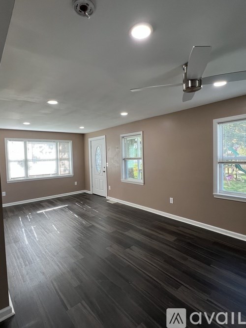 A room with a ceiling fan and light fixture, and a dark wood floor.
