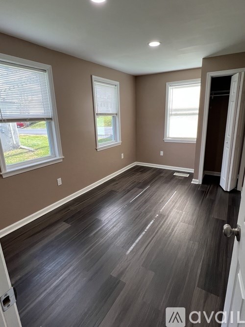 A room with wooden flooring and two windows.
