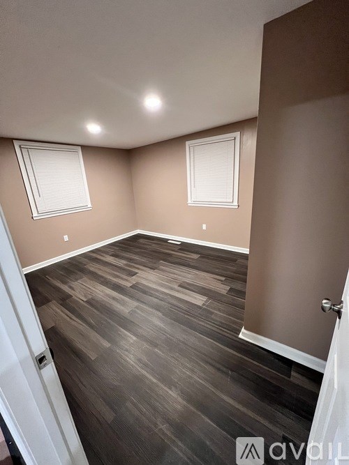 A room with wooden flooring and two windows.